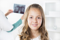 Jente som ser mot kameraet og tannpleier som står bak med et røntgenbilde
