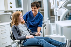 Tannhelsesekretær holder barn som sitter i tannlegestolen i hånden. 